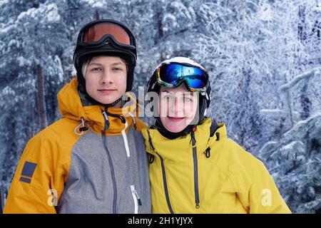 Ritratto invernale di persone felici di etnia caucasica in caschi da sci e occhiali. Donna e suo figlio sullo sfondo di una foresta innevata. Famiglia Foto Stock