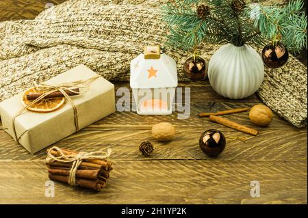 Composizione dell'anno nuovo con scatole regalo fatte di mestiere, una candela in una torcia a candeliere, un maglione caldo a maglia, noci, cannella, fette d'arancia Foto Stock