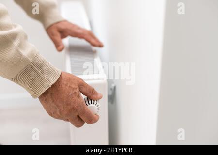 Un uomo anziano scalda le mani su un riscaldatore elettrico. Nella bassa stagione, il riscaldamento centralizzato è ritardato, in modo da la gente deve comprare i riscaldatori supplementari a. Foto Stock