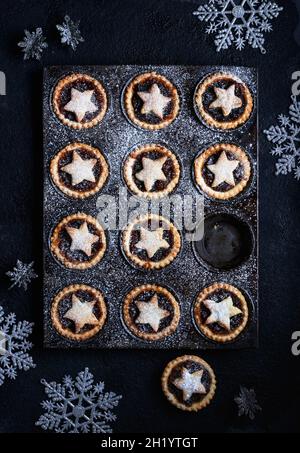 Un vassoio di torte tritate decorate con stelle impolverate con zucchero a velo su sfondo scuro con decorazioni natalizie Foto Stock