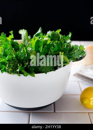 Broccolini in una ciotola bianca, con un limone e un blocco di parmigiano Foto Stock