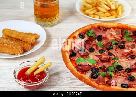 Pizza in primo piano su un piatto su un tavolo di legno bianco con ketchup, succo di frutta, salsa e patate. Foto Stock