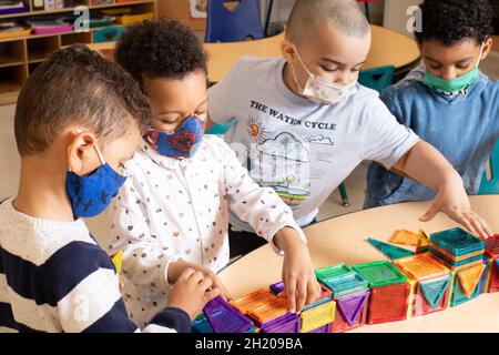 Istruzione Preschool 3-4 anni quattro ragazzi che giocano con le tessere magnetiche, tutti indossando maschere per proteggere contro il covid-19 Foto Stock