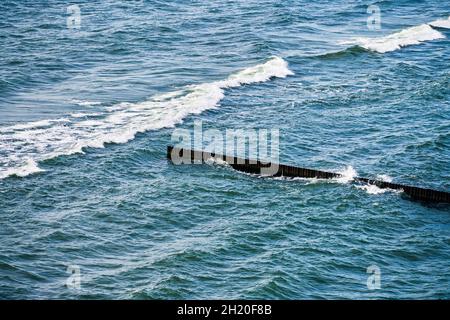 Vintage lungo groynes in legno che si estende lontano verso le acque del mare, vista panoramica del mare blu aperto con onde schiumose. Le onde si infrangono contro le frangiflutti. BEA Foto Stock