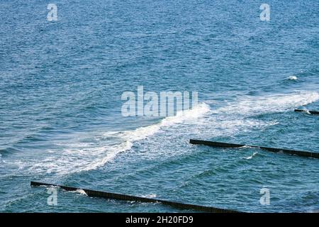 Vintage lungo groynes in legno che si estende lontano verso le acque del mare, vista panoramica del mare blu profondo con onde schiumose. Le onde si infrangono contro le frangiflutti. BEA Foto Stock