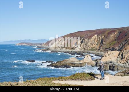 Una donna in piedi vicino al bordo della scogliera si affaccia sull'acqua, a Bodega Head, California. Foto Stock