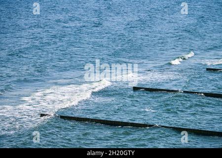 Vintage lungo groynes in legno che si estende lontano verso le acque del mare, vista panoramica del mare blu aperto con onde schiumose. Le onde si infrangono contro le frangiflutti. BEA Foto Stock