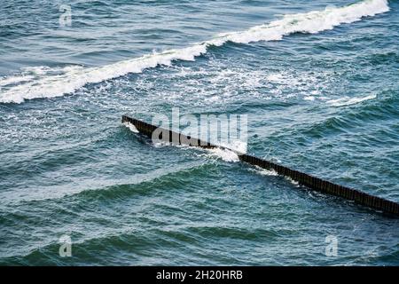 Vintage lungo groynes in legno che si estende lontano verso le acque del mare, vista panoramica del mare blu profondo con onde schiumose. Le onde si infrangono contro le frangiflutti. BEA Foto Stock