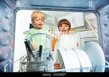 Due ragazzi prendono i piatti dalla lavastoviglie in cucina Foto Stock