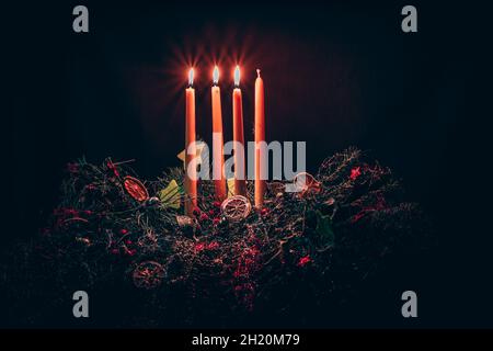 3 candele lucenti sulla corona dell'avvento decorata a colori con quattro candele su sfondo nero Foto Stock