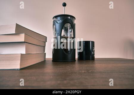 macchina da caffè french press e si riempie a metà di caffè arabo e nero insieme a una caffettiera nera con un pacchetto di libri. Foto Stock
