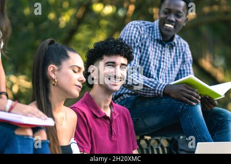 Uomo moderno sorridente seduto su una panchina accanto ad un gruppo multietnico di amici Foto Stock