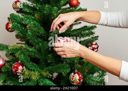 Primo piano delle mani di una donna che decorano un albero di natale Foto Stock