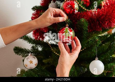 Primo piano delle mani di una donna che decorano un albero di natale Foto Stock