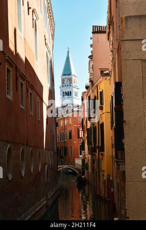 Vista di uno stretto canale circondato da vecchie case in mattoni, con la cima del Campanile di San Marco sul retro. Foto Stock