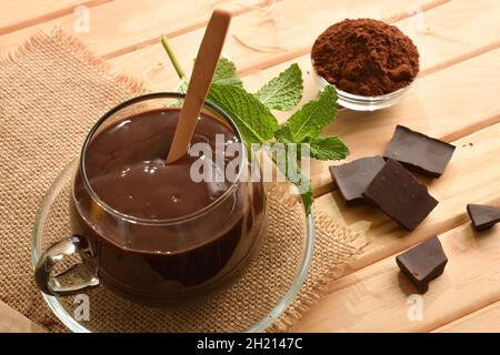 Cioccolata calda in Country crema di cioccolato in bicchiere di vetro su tavoletta di legno con pezzo e polvere di cioccolato. Vista rialzata. Composizione orizzontale. Foto Stock