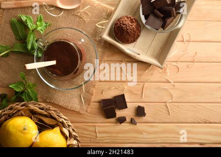 Crema di cioccolato caldo in bicchiere su tavoletta di legno con pezzetto e polvere di cioccolato. Vista rialzata. Composizione orizzontale. Foto Stock