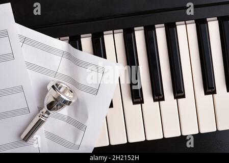 Strumenti in ottone e concerto di pianoforte con sfondo di boccaglio su tasti pianoforte e lenzuola dello staff. Vista dall'alto. Composizione orizzontale. Foto Stock