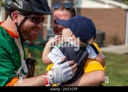 Columbus, OH USA 08-07-2021: Primo piano immagine isolata di una giovane famiglia caucasica di tre con bambino in braccia di mamma e papà che partecipa a una spora ciclistica Foto Stock