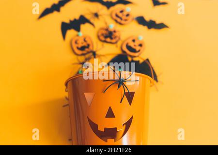 Buon Halloween. Secchio della lanterna del jack o con ragni, pipistrelli e zucche su sfondo arancione vista dall'alto. Trick o delizia. Decorazioni di Halloween su giallo Foto Stock