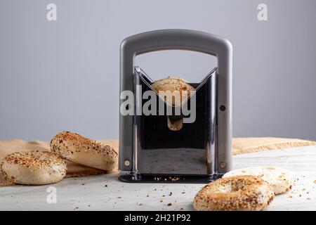 primo piano immagine isolata che mostra i bagel sessame appena sfornati sul piano di lavoro della cucina con un affettatore di bagel al centro. Un bagel viene affettato Foto Stock