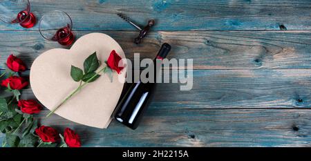 San Valentino sfondo vacanza con rose rosse, bottiglia di vino, bicchieri da bere e grande scatola regalo a forma di cuore su tavole di legno blu sbiadito Foto Stock