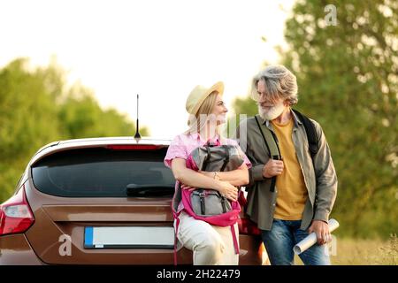 Coppia matura felice con zaini e mappa vicino auto in campagna Foto Stock