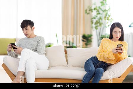 Giovane coppia seduta sul divano usando lo smartphone e ignorandosi l'un l'altro. Foto Stock