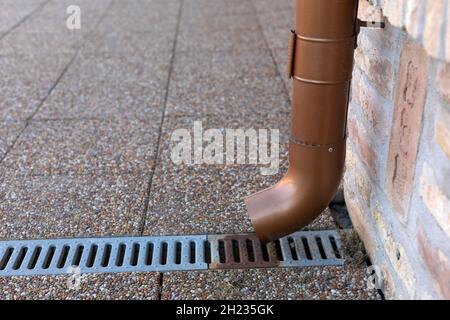 Downpipe di acqua piovana in metallo color bronzo con una griglia di drenaggio su un marciapiede in pietra Foto Stock