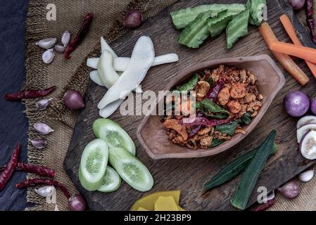 Crackling di maiale Chili Paste con foglie di lime di kaffir fritte con l'ingrediente e verdure fresche su sfondo di legno, vista dall'alto. Foto Stock