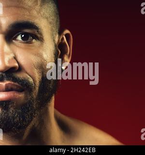 Faccia con una barba e un orecchino nell'orecchio di un uomo cubano primo piano. Ritratto da studio di un uomo brutale. Foto Stock