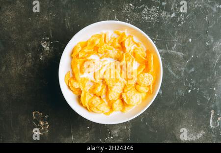 Gustosi fiocchi di mais croccanti con latte in ciotola sullo sfondo rustico. Messa a fuoco selettiva. Profondità di campo poco profonda. Foto Stock