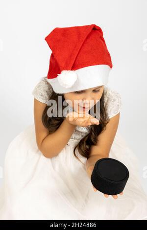 Ritratto di dolce, gioiosa ragazza in cappello Babbo Natale soffia un bacio a altoparlante di musica intelligente, isolato su sfondo bianco, concetto di bambini Capodanno Foto Stock