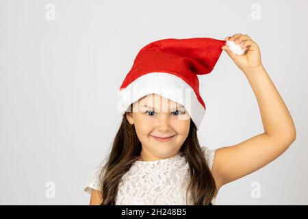 Primo piano ritratto di carina, bella ragazza con capelli lunghi in rosso Santa cappello che tiene pompom con mano, isolato su sfondo bianco Foto Stock