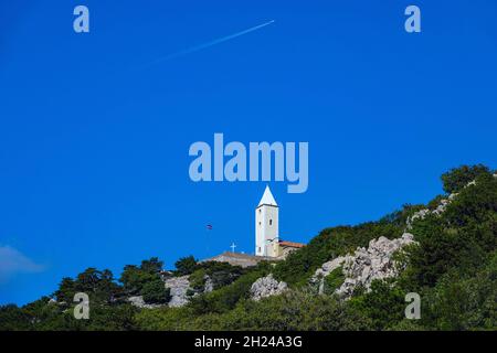 La torre bianca della chiesa contro il cielo blu con l'aeroplano contrail, alla piccola località turistica di Baska, Baška sull'isola di Krk, Croazia Foto Stock