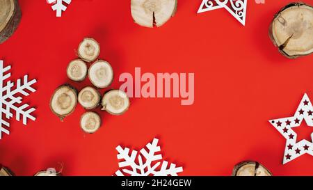 Tagli di legno o branche, disposti a forma di albero di Natale con fiocchi di neve in legno su sfondo rosso. Banner. Disposizione piatta. Spazio di copia Foto Stock