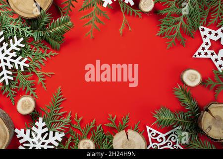 Tagli di legno o bramme di ramo e fiocchi di neve di legno con rami di albero di Natale su sfondo rosso. Natale o Capodanno. Disposizione piatta. Spazio di copia Foto Stock