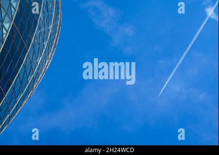 Un aeroplano ad alta quota che affetta il cielo sopra la città di Londra con contrail, più una sezione dell'edificio Gherkin mostrato. Londra, Inghilterra. Foto Stock