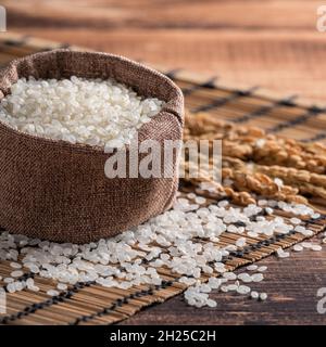 Riso bianco crudo macinato commestibile su fondo tavola di legno in una ciotola, concetto di design organico. Foto Stock