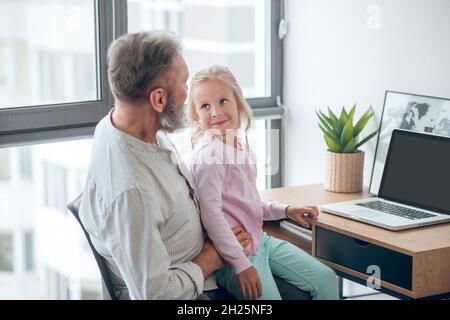 Un uomo d'affari seduto al tavolo e che tiene sua figlia piccola Foto Stock