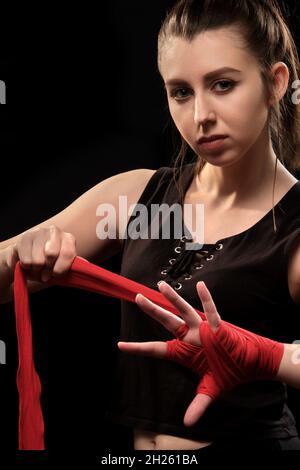 Muay Thai femmina boxer con cinturino al polso. Fitness giovane donna con corpo muscolare che si prepara per l'allenamento di boxe su sfondo nero Foto Stock