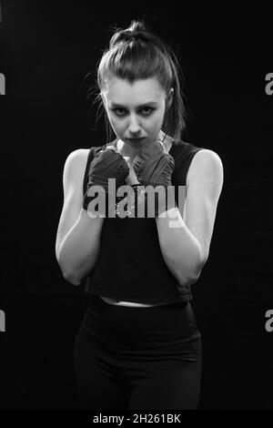 Arrabbiato Muay tailandese pugile in posa di attacco. Fitness giovane donna pugilato formazione su sfondo nero, closeup monocromatico Foto Stock