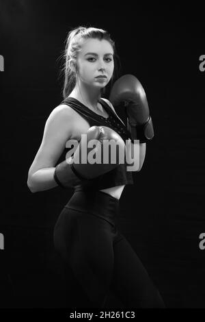 Arrabbiato Muay tailandese pugile in posa di attacco. Fitness giovane donna pugilato formazione su sfondo nero, closeup monocromatico Foto Stock