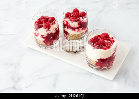 Tre bicchieri riempiti di dessert al lampone fatto in casa su tavola di marmo bianco e sfondo di marmo bianco con molto spazio per le copie. Vista ad angolo alto. Foto Stock