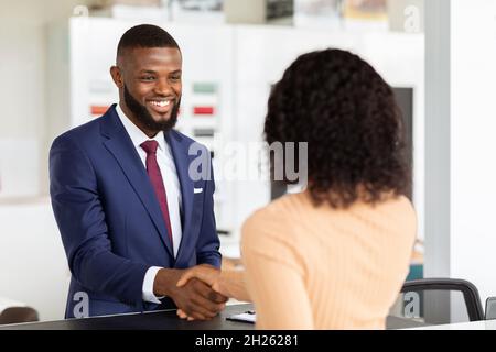 Il venditore di auto sorridente agita le mani con il cliente femminile dopo un affare riuscito Foto Stock