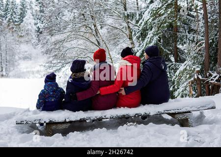 famiglia grande, genitori e tre bambini sono seduti su una panca in una panca nevosa foresta. Foto Stock