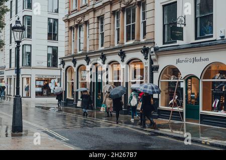 Londra, Regno Unito - 02 ottobre 2021: Le donne che tengono gli ombrelli camminano oltre Harvie e Hudson, un negozio per uomo che vende abiti classici alla moda, cravatte, camicie d'abbigliamento e. Foto Stock