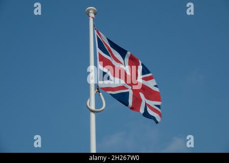 Una bandiera union jack che vola da una bandiera bianca palo contro un cielo blu Foto Stock