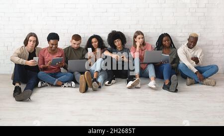 Gruppo internazionale di giovani che utilizzano diversi gadget Foto Stock