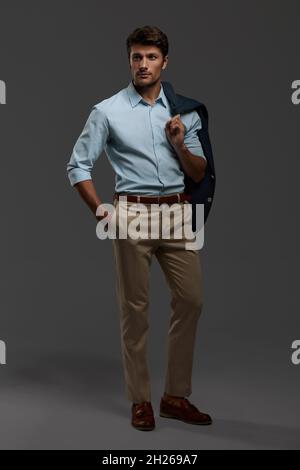 Giovane bel uomo d'affari europeo focalizzato. Vista frontale di uomo bearded con capelli scuri indossare abiti formali. Isolato su sfondo grigio scuro. Studio s Foto Stock